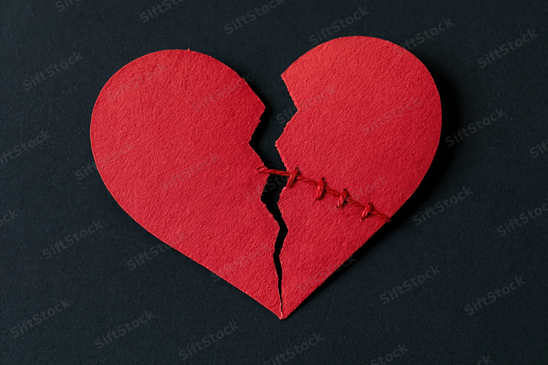 Red paper heart cut in half and stitched back together on black surface