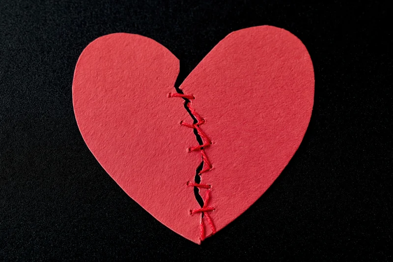 Red paper heart cut in half and stitched back together on black surface