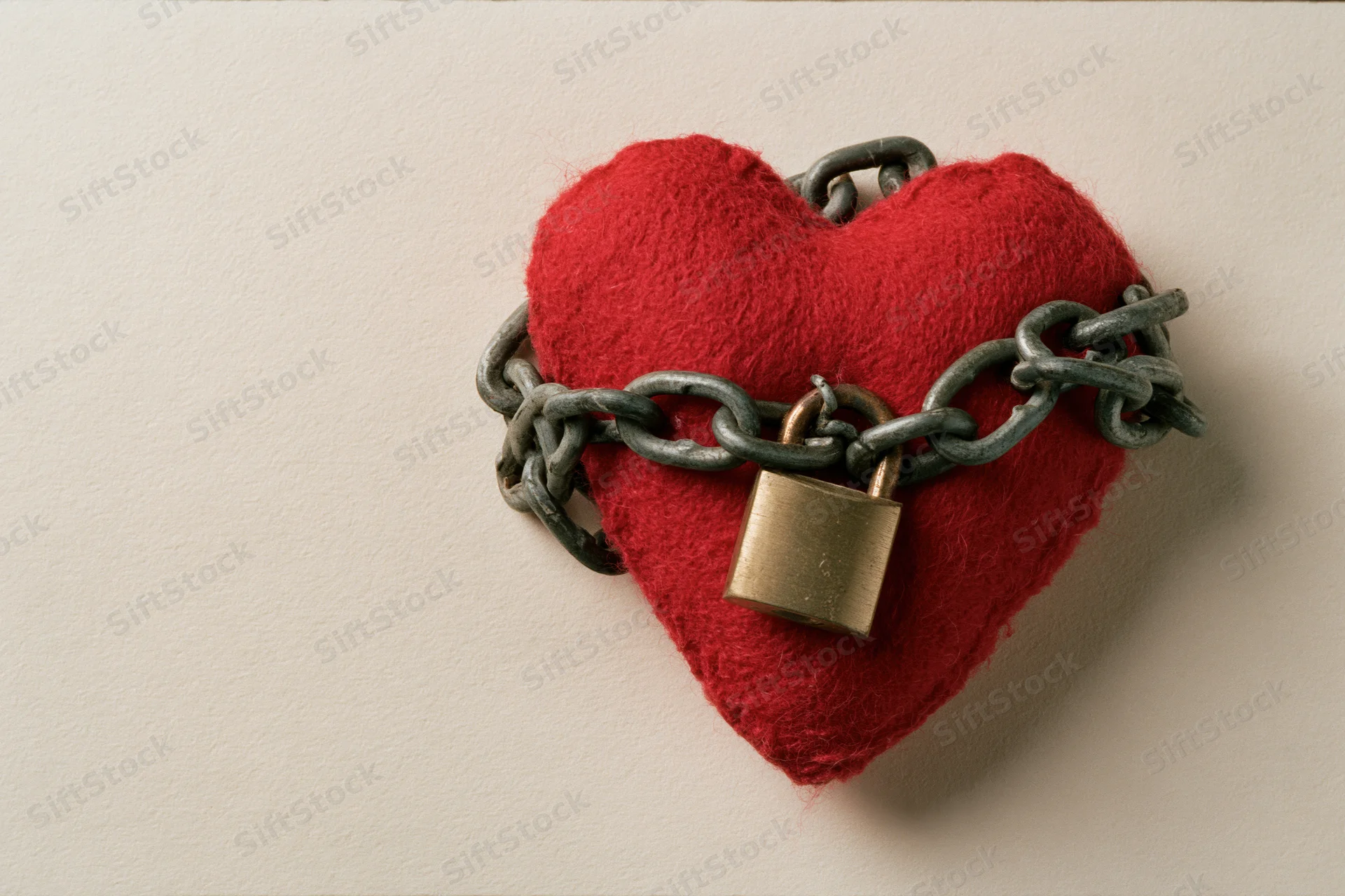 Red fabric heart wrapped in metal chain with brass padlock on white surface