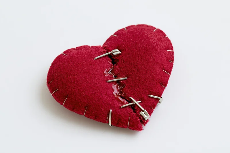 Red felt heart with staples and stitching repairing a split seam on white background