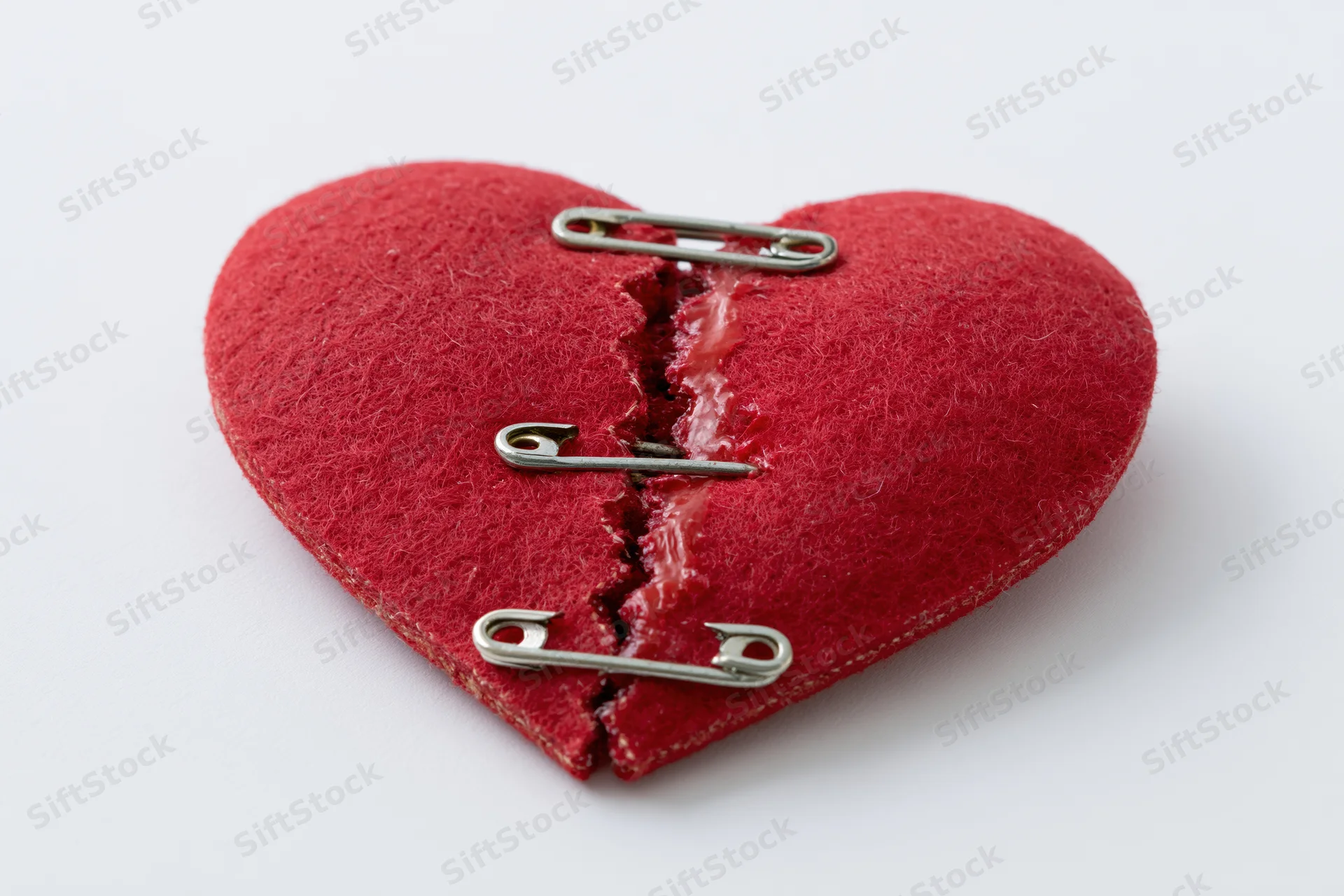 Red felt heart split and mended with safety pins on white background