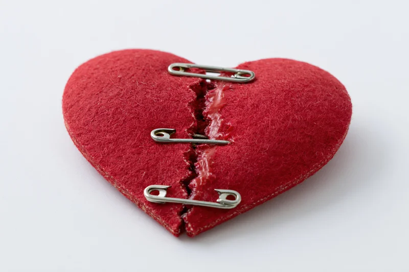 Red felt heart split and mended with safety pins on white background