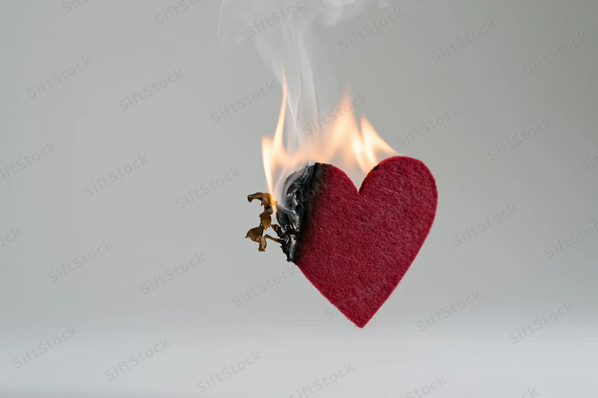 Red felt heart cutout burning with flame and smoke against white background