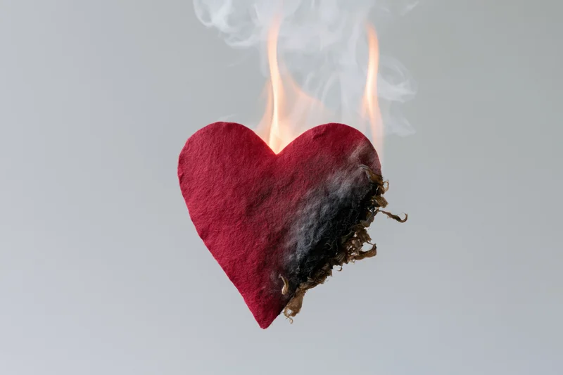Red felt heart burning with flame and smoke against white background