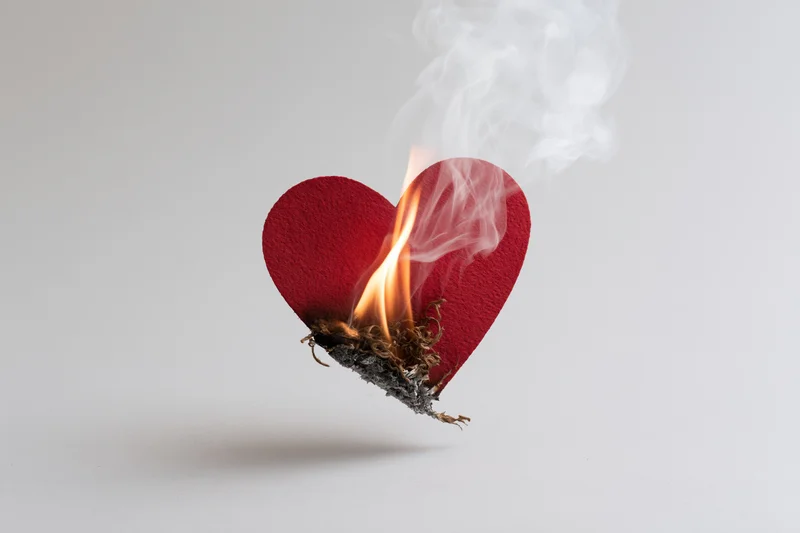 Red felt heart cutout burning with flame and smoke on white background
