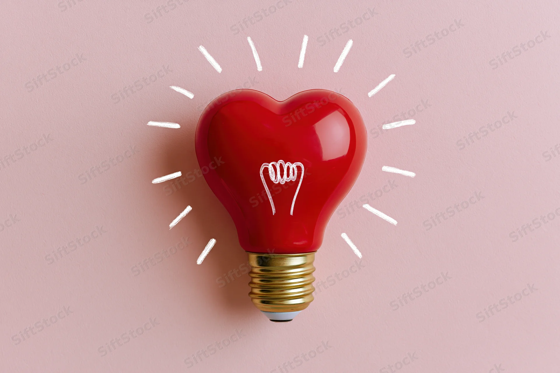 Red heart-shaped lightbulb with gold base and white glow lines on pink background