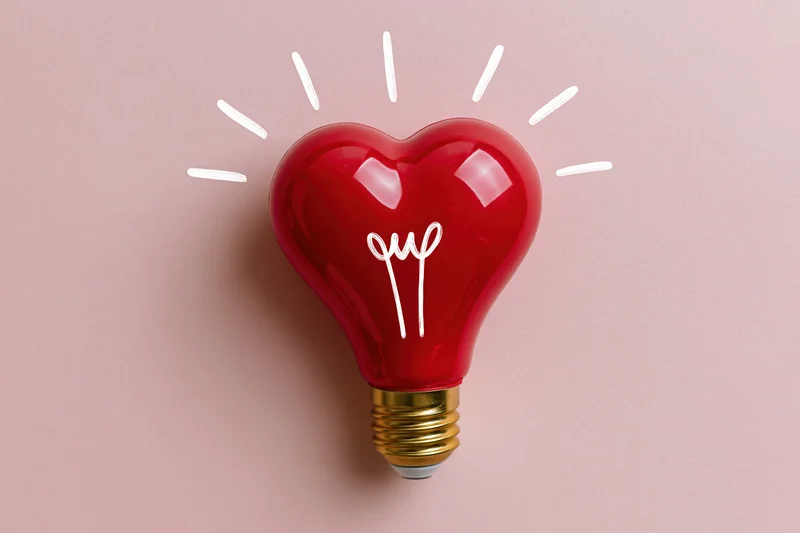 Red heart-shaped lightbulb with gold base on pink surface