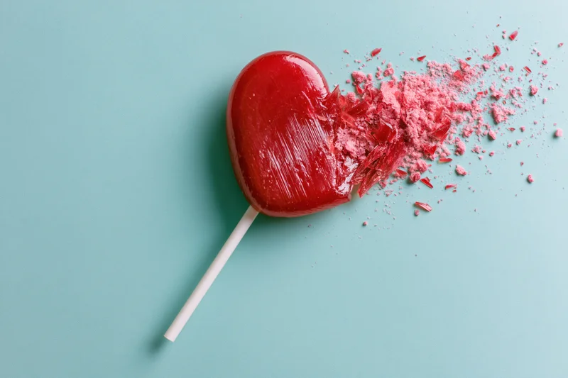 Broken red heart-shaped lollipop with shattered pieces on turquoise background