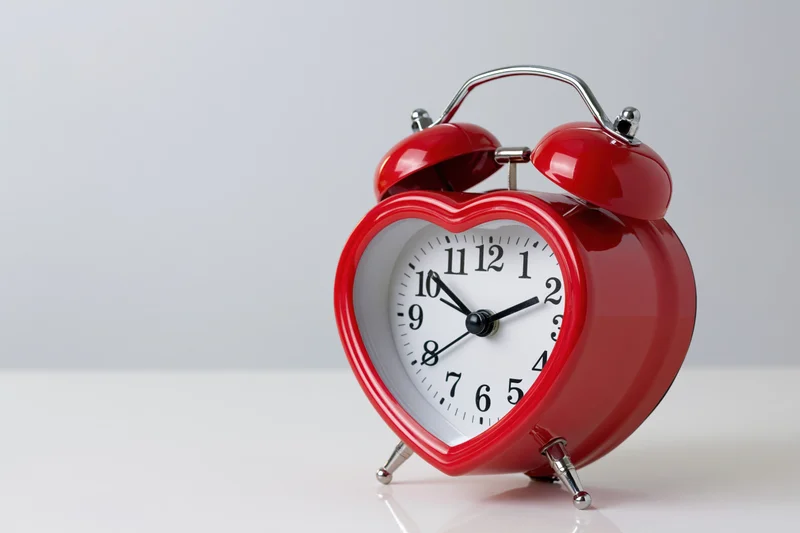 Red heart-shaped twin-bell alarm clock on white surface