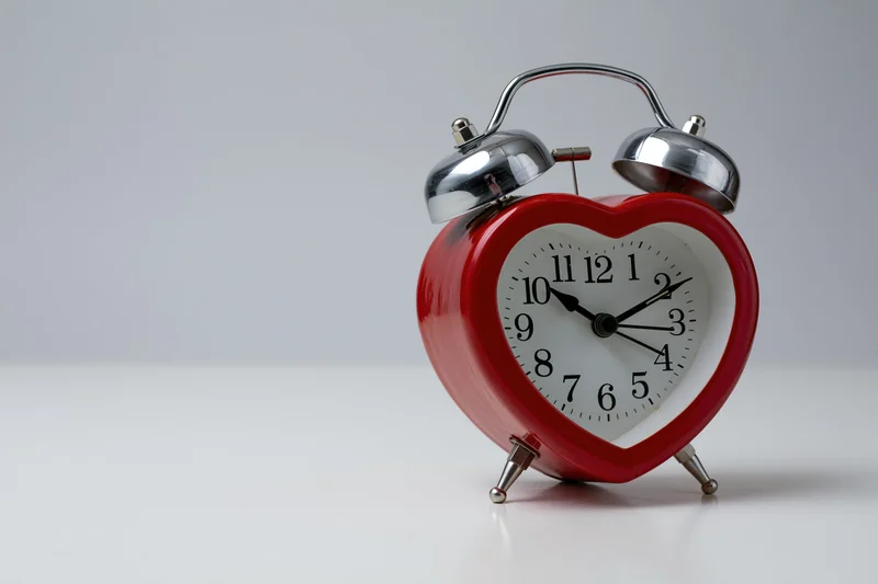 Red heart-shaped alarm clock with twin bells on white surface