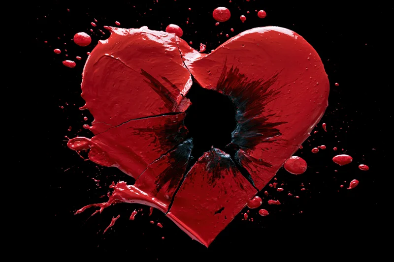 Broken red paint heart with shattered hole and splatters on black background