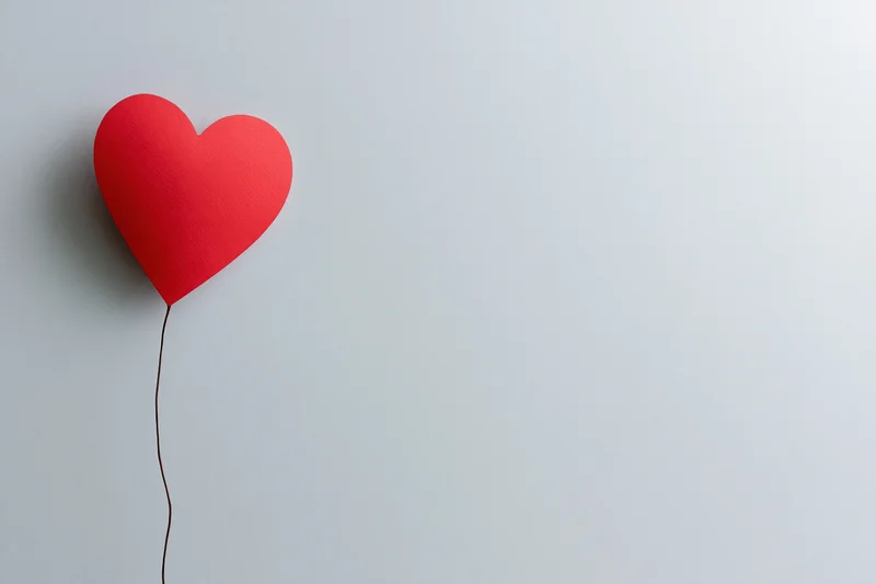 Red paper heart cutout floating on a white surface with string attached