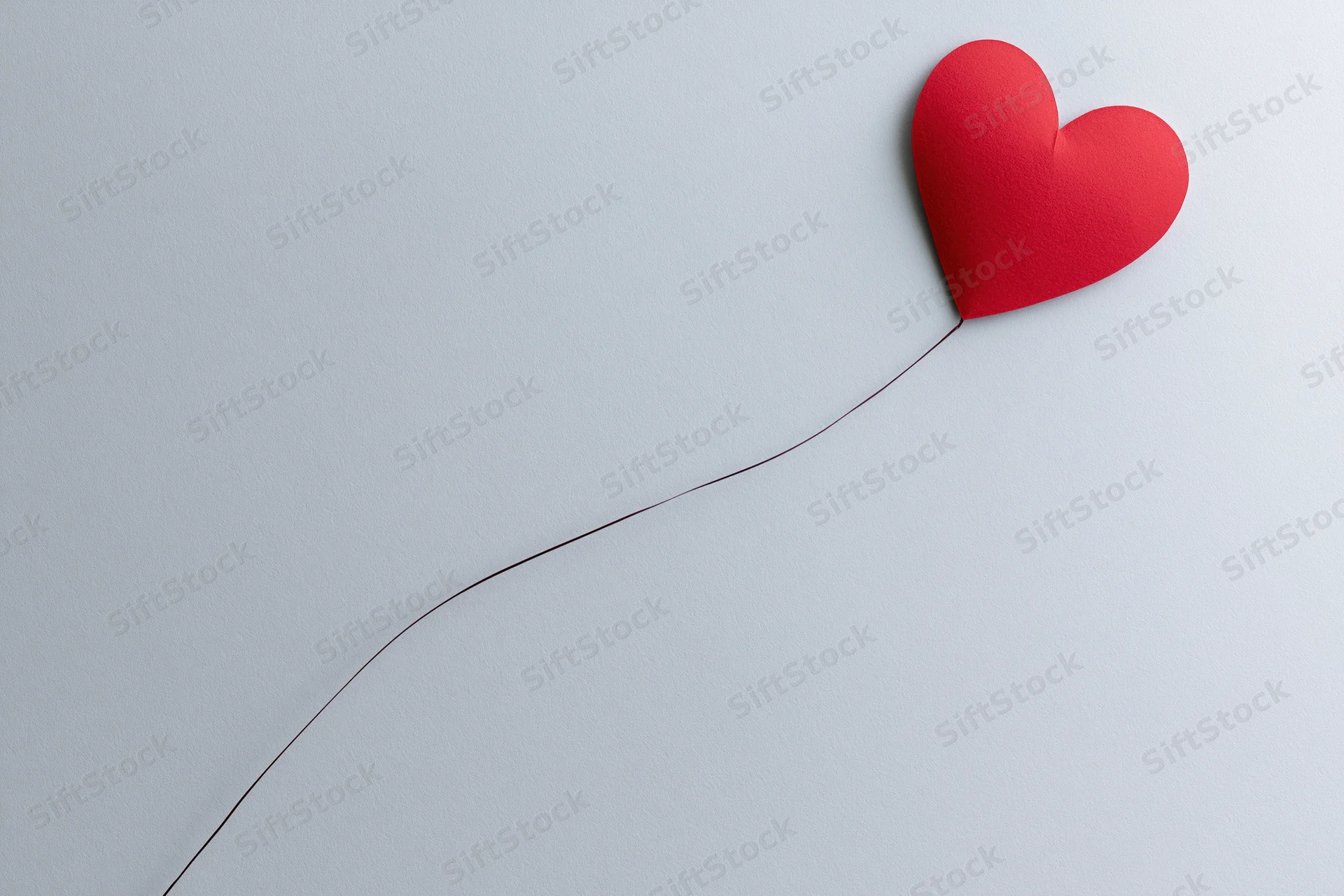 Red paper heart cutout with string on white background