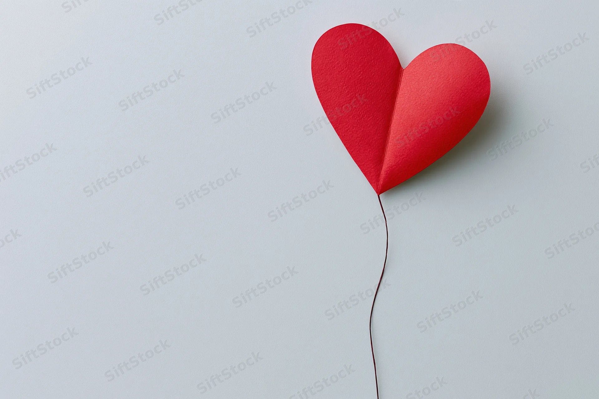 Red paper heart cutout on light gray background with string attached, positioned in upper right corner