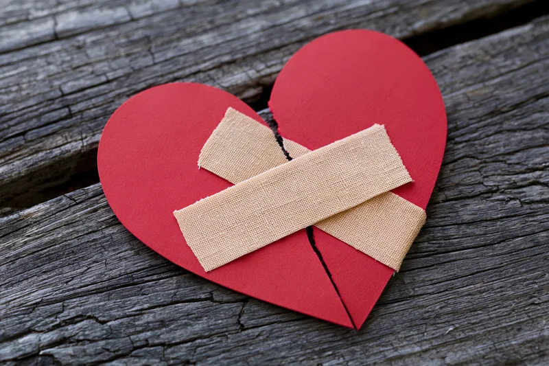 Broken red paper heart mended with bandages on weathered wood