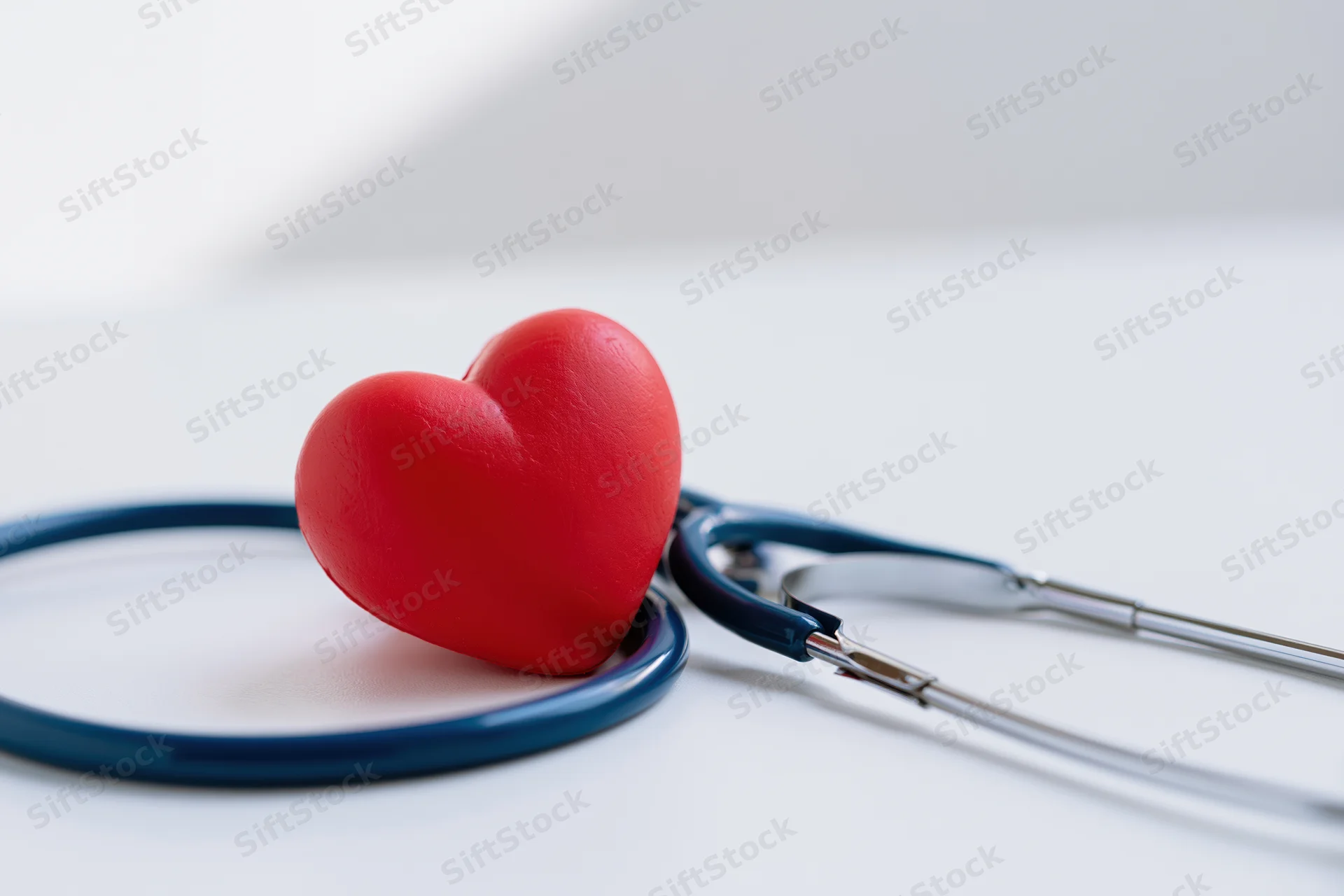 Red heart toy resting against blue stethoscope on white surface