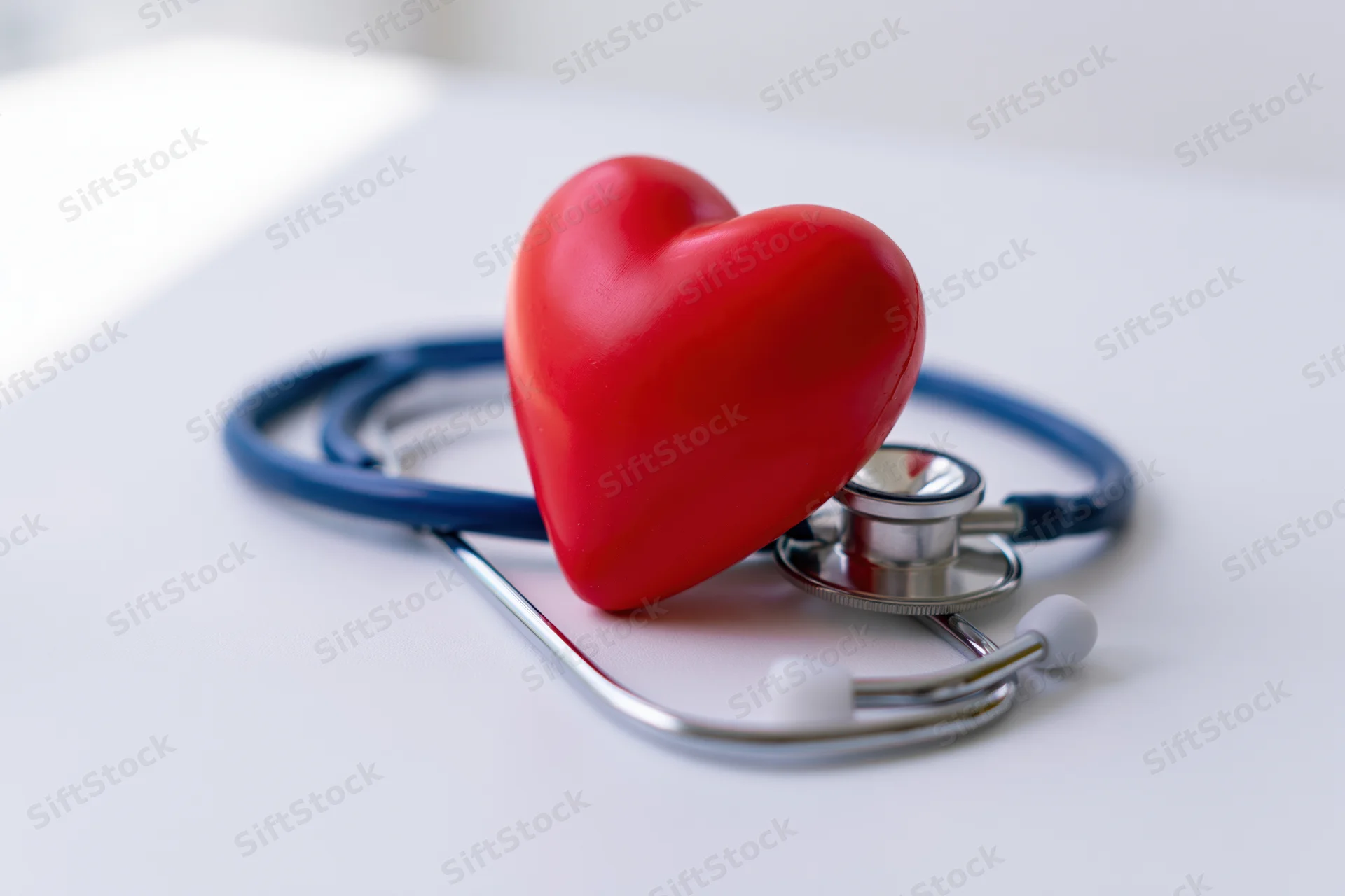 Red heart toy resting on blue stethoscope on white surface