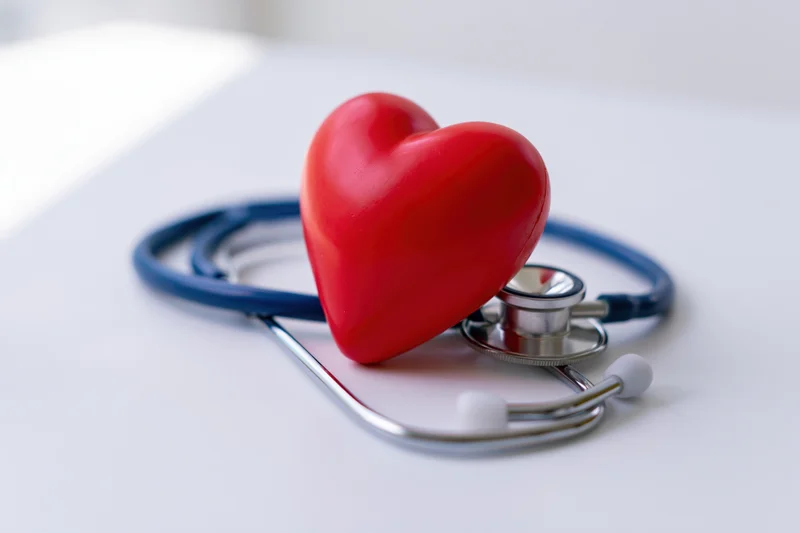 Red heart toy resting on blue stethoscope on white surface