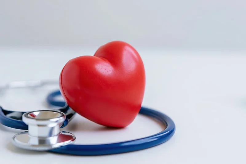 Red heart toy resting on blue stethoscope on white surface