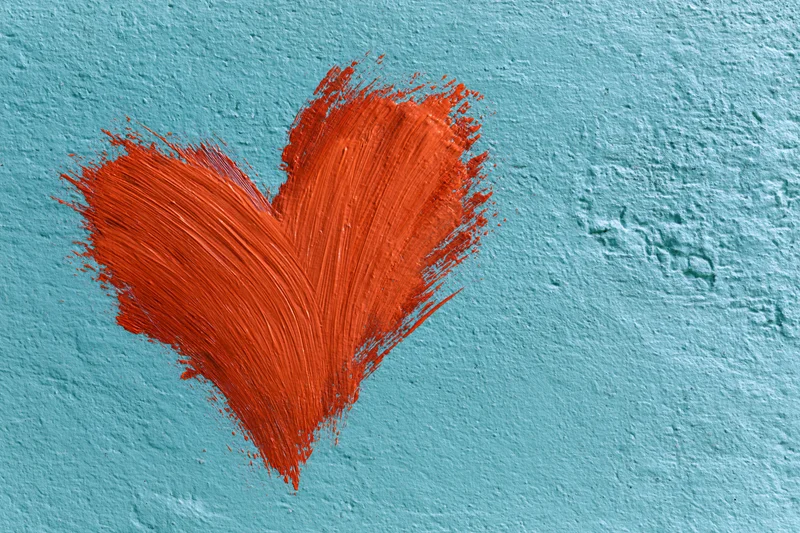 Red painted heart with visible brushstrokes on textured turquoise concrete wall