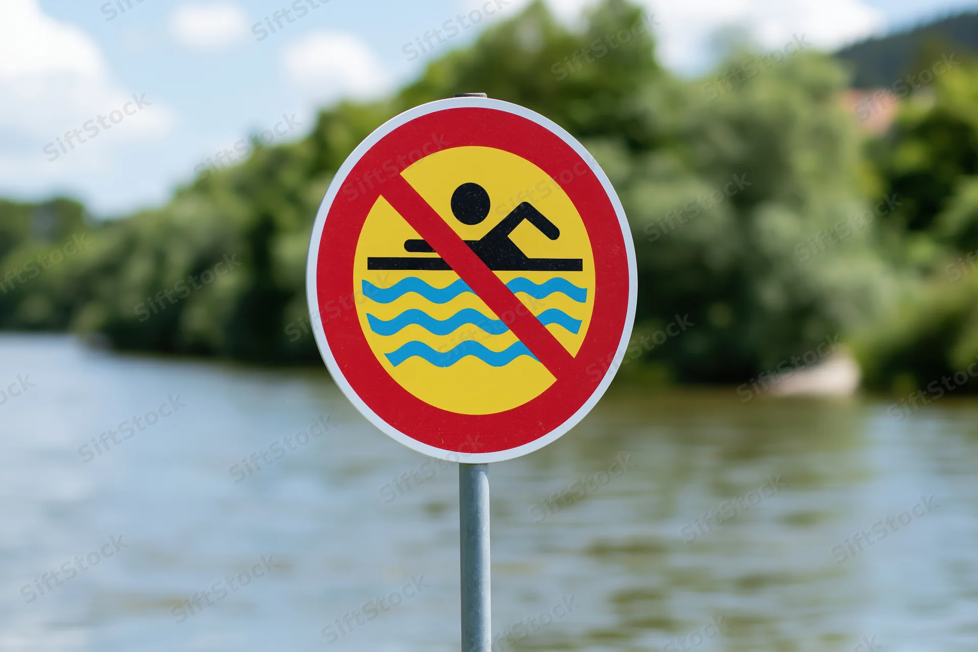 Round prohibition sign forbidding swimming near a river with trees and sky in background