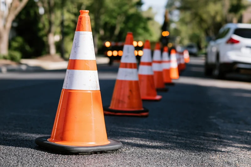 Row of orange traffic cones with white reflective bands lining a street during daytime roadwork