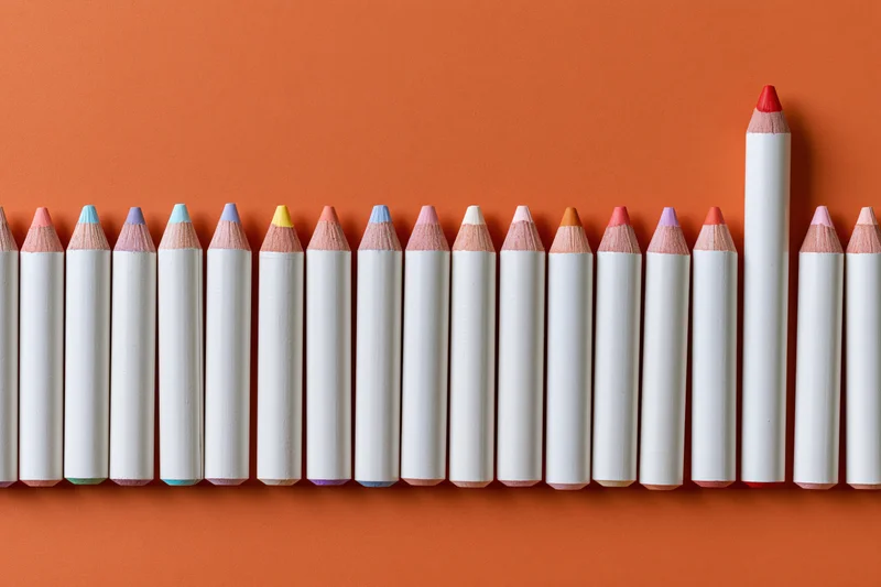 Row of white colored pencils with multicolored tips arranged horizontally on orange background