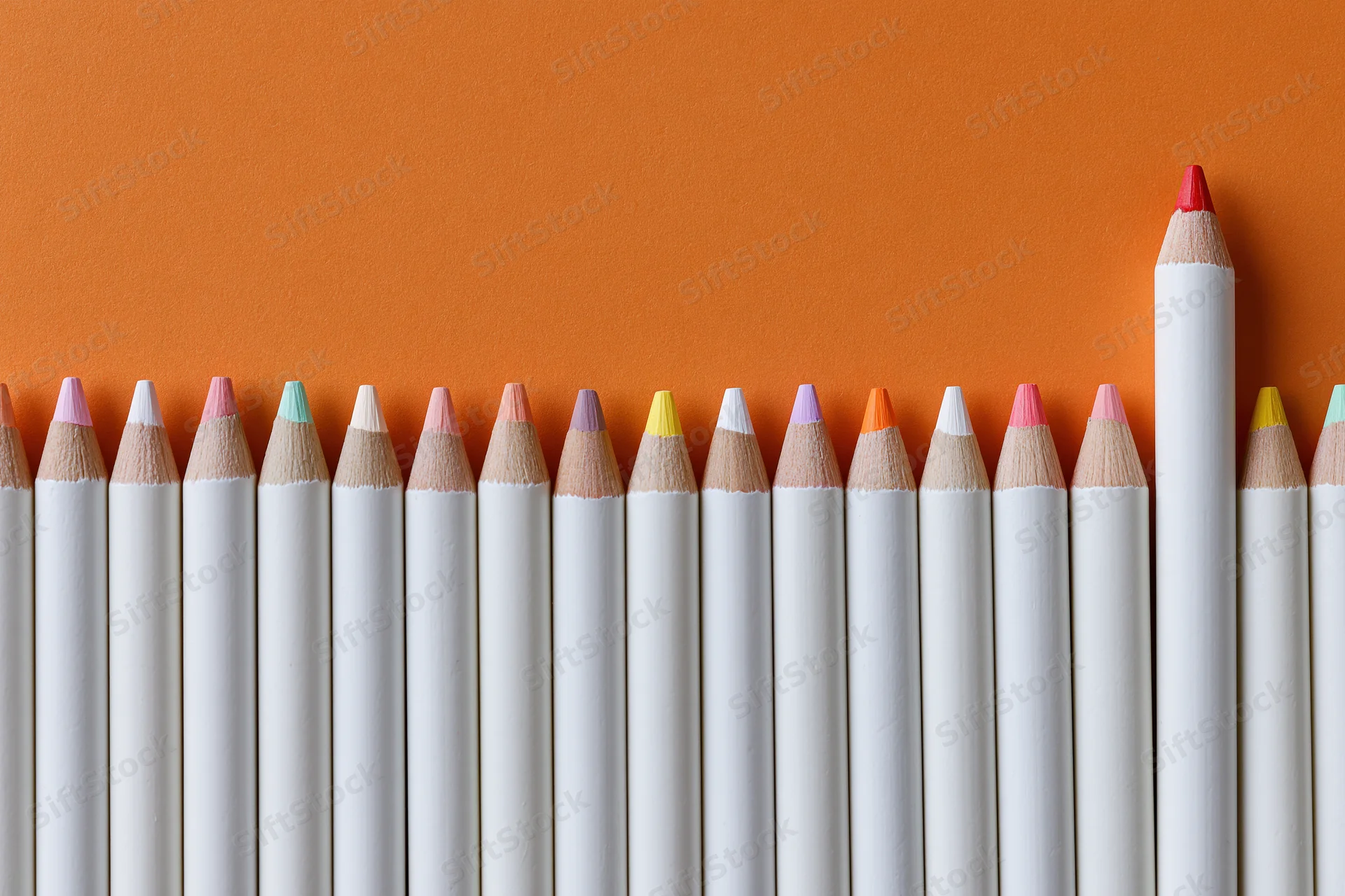 Row of white colored pencils with multicolored tips arranged in a line against orange background