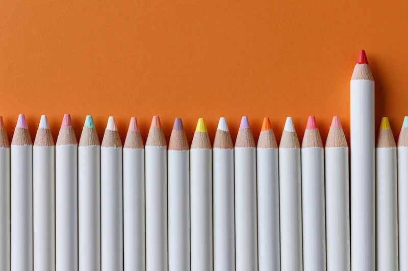 Row of white colored pencils with multicolored tips arranged in a line against orange background