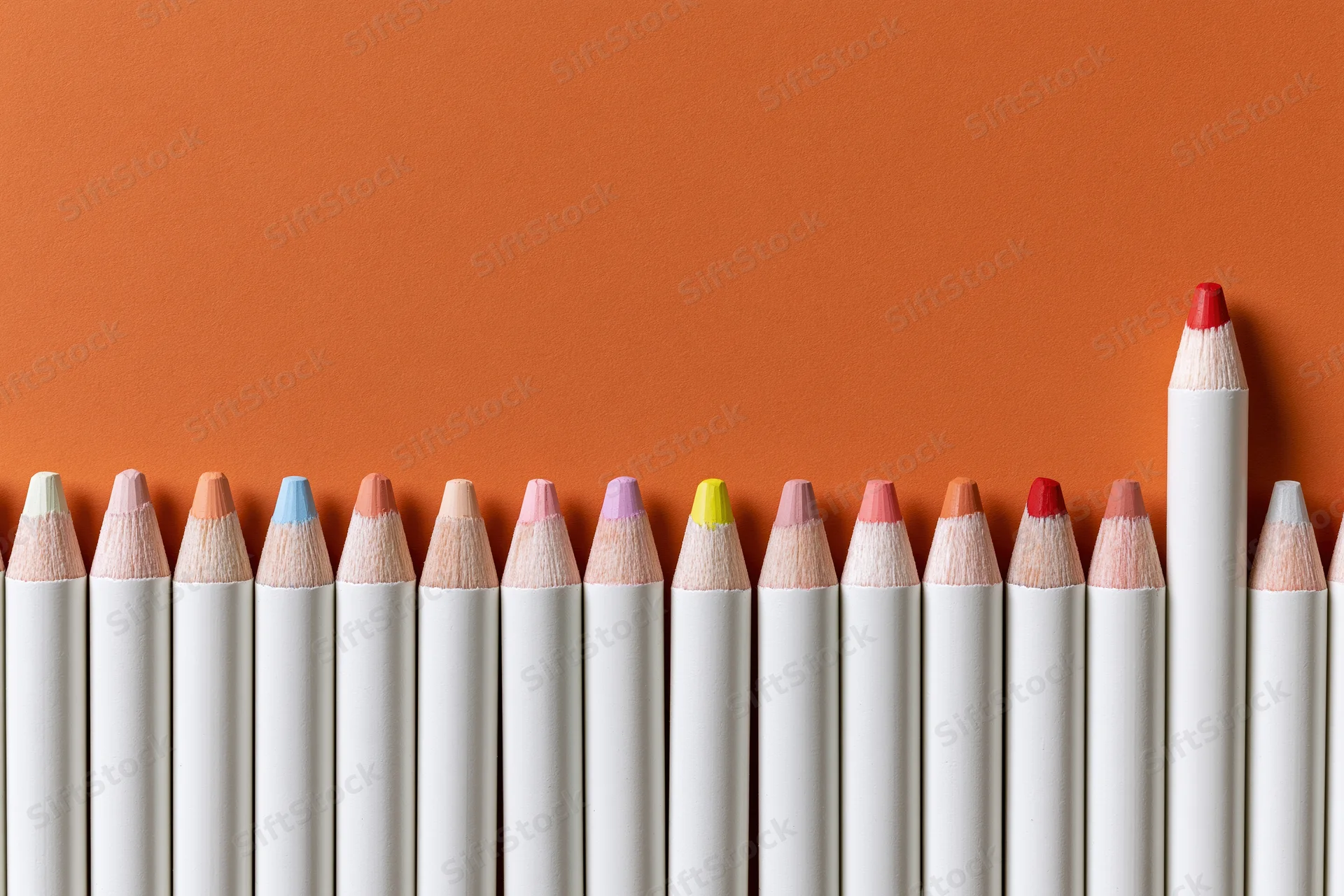 Row of white colored pencils with multicolored tips arranged in a line against orange background