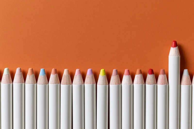 Row of white colored pencils with multicolored tips arranged in a line against orange background