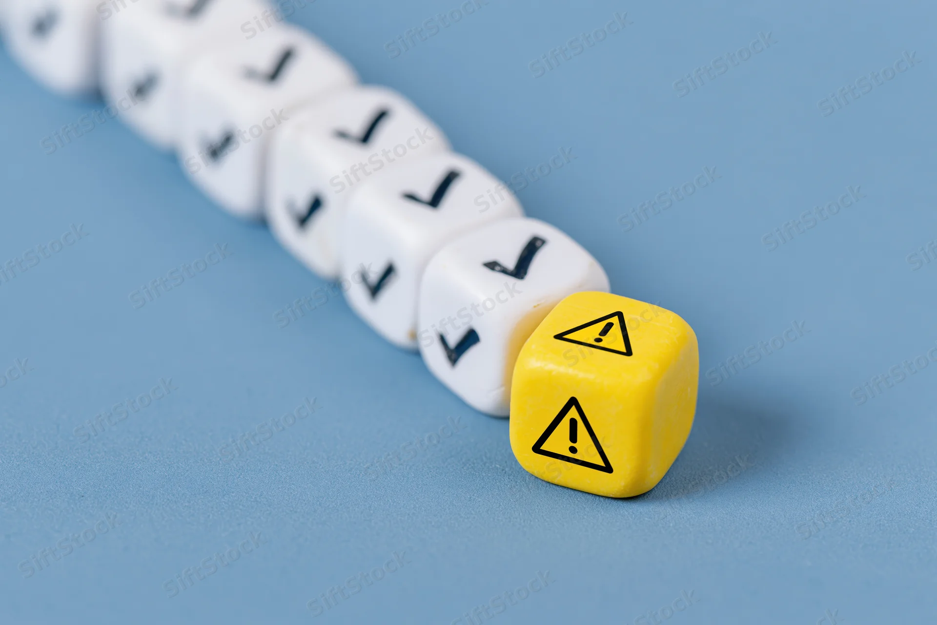 Row of white dice with checkmarks and one yellow warning die on blue surface