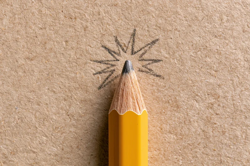 Sharp yellow pencil pointing upward with a hand-drawn starburst on textured brown paper