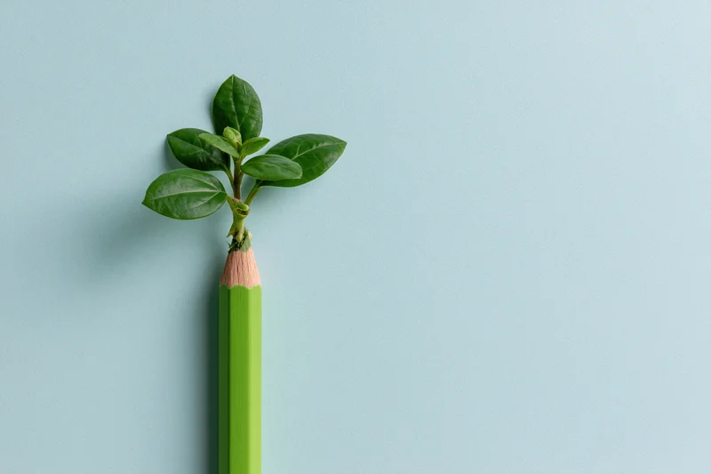 Green pencil with small plant growing from tip against light blue background