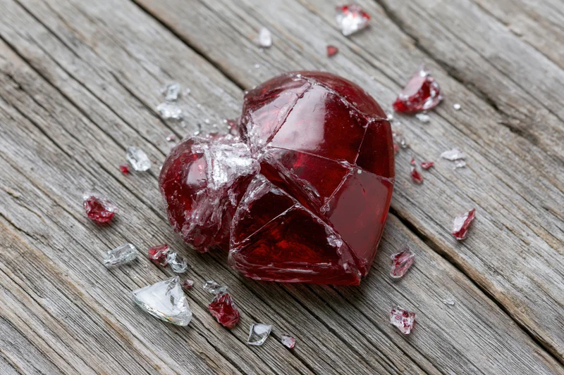 Shattered red glass heart with fragments on weathered wooden surface