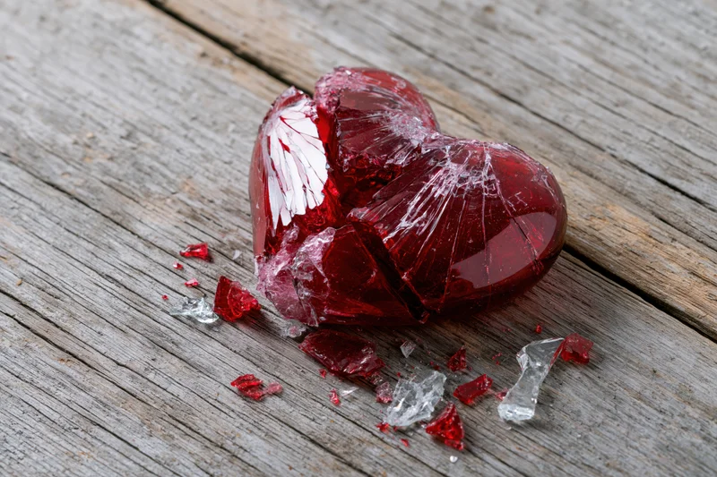 Shattered red glass heart lying on weathered wooden surface