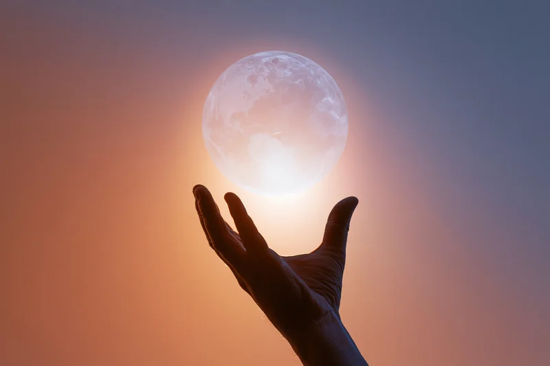 Silhouetted hand reaching toward a glowing moon in a twilight sky