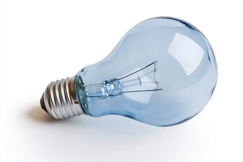 Blue-tinted incandescent light bulb lying on white surface with visible filament and screw base
