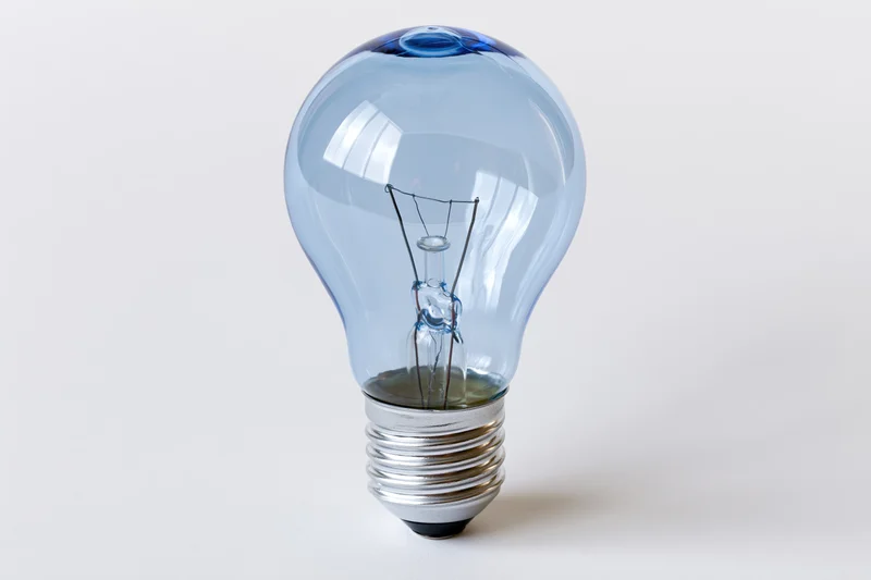 Blue-tinted incandescent light bulb with visible filament and metal screw base on white background