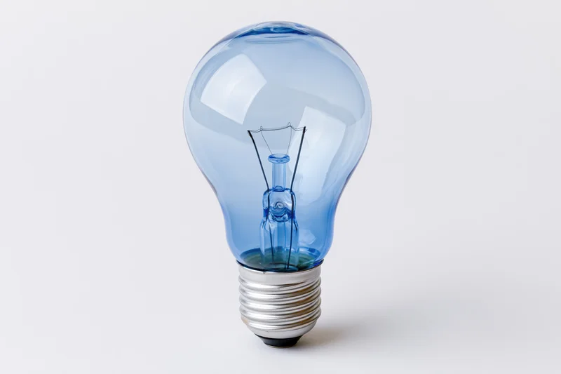 Blue-tinted incandescent lightbulb on white background with copyspace