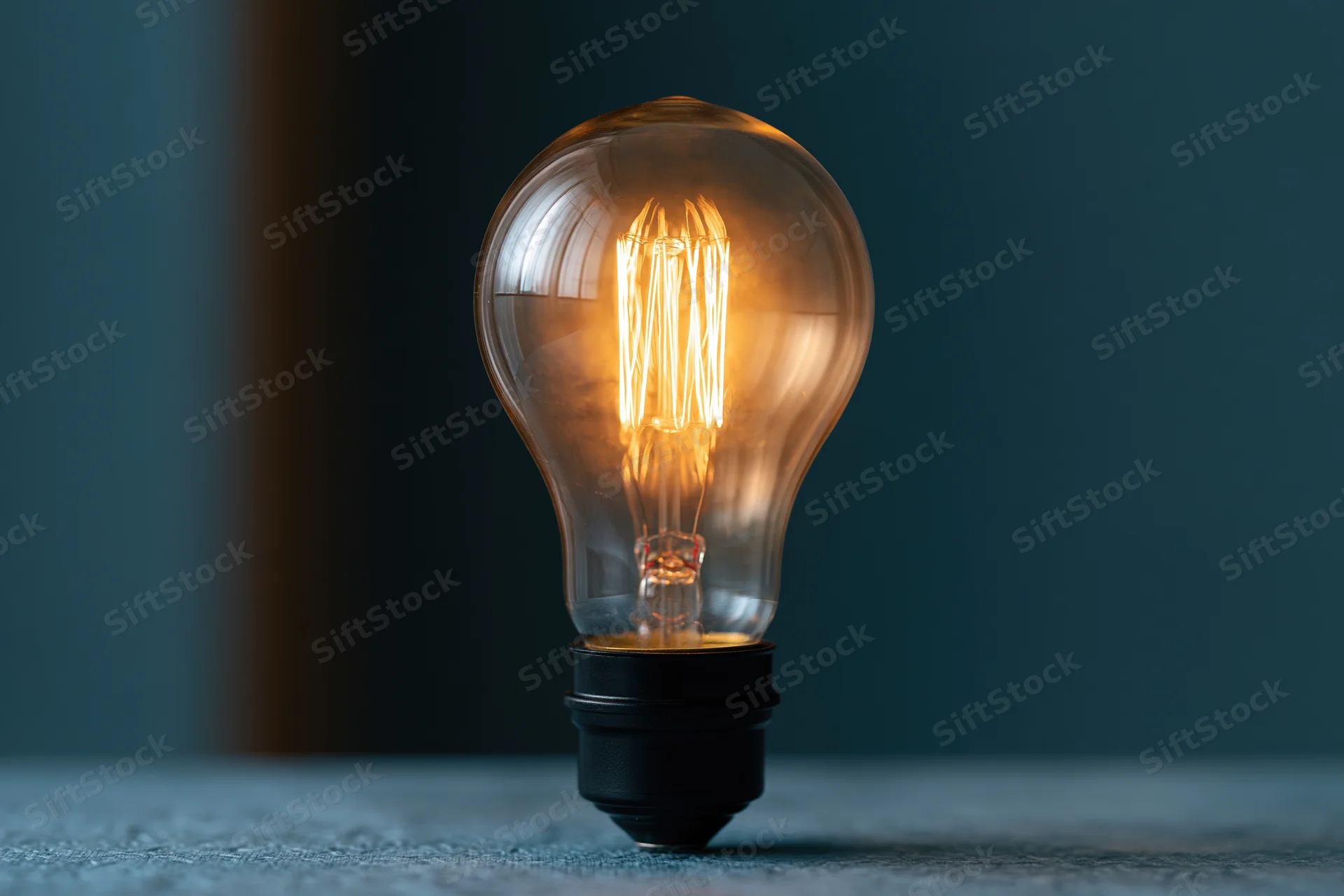 Glowing incandescent lightbulb with visible filament on a dark surface