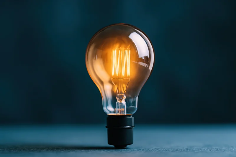 Glowing incandescent lightbulb with visible filament on dark blue surface