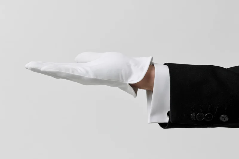 Gloved hand extended palm up in formal suit sleeve against plain background