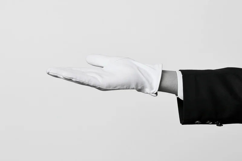Gloved hand extended palm up in formal suit sleeve against plain background