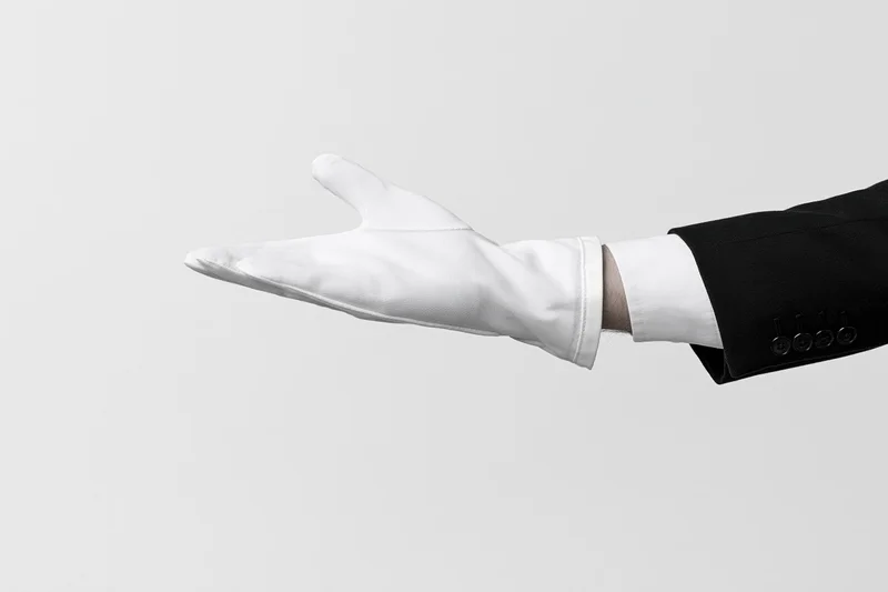 Gloved hand extended palm up in formal suit sleeve against white background