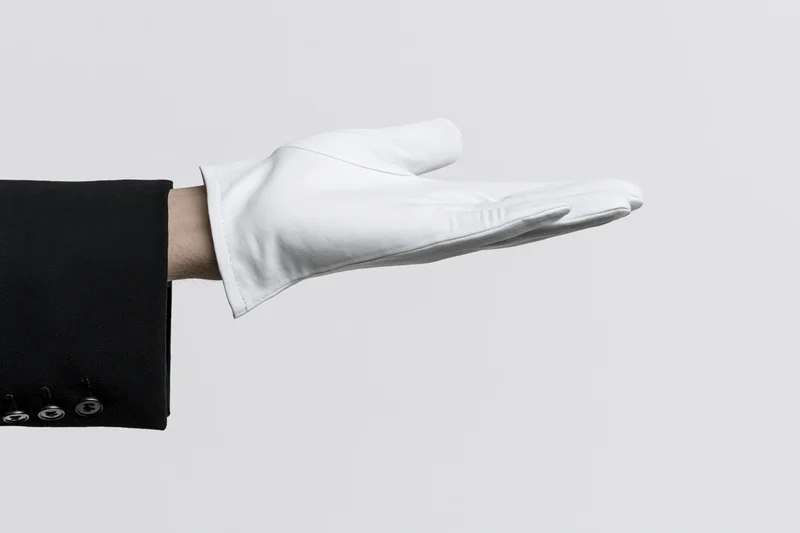 Gloved hand extended palm up in formal suit sleeve against white background