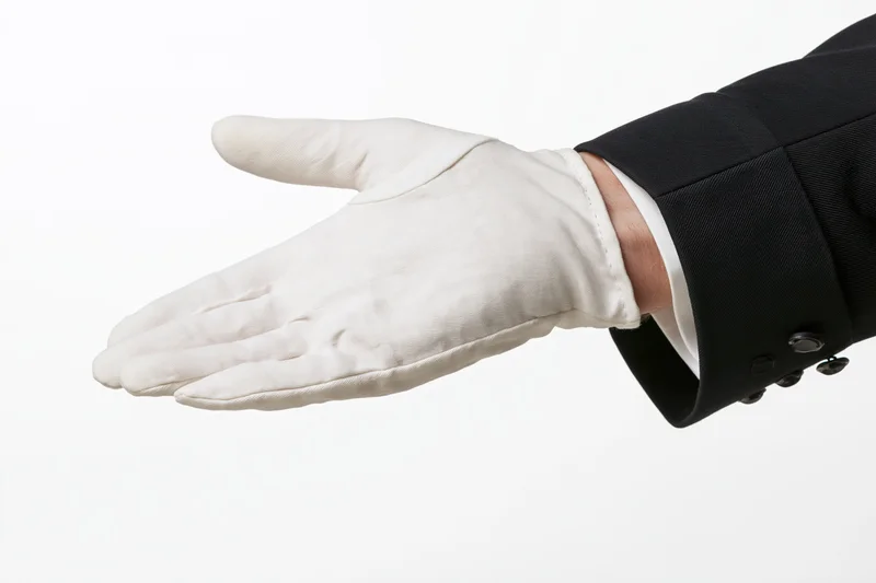 Gloved hand extended palm up in formal suit sleeve against white background