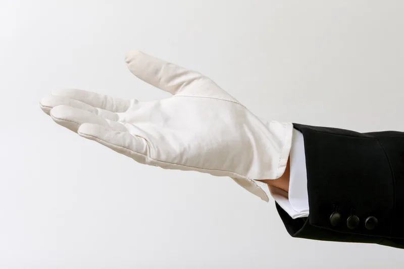 Gloved hand extended palm up in formal suit sleeve against white background