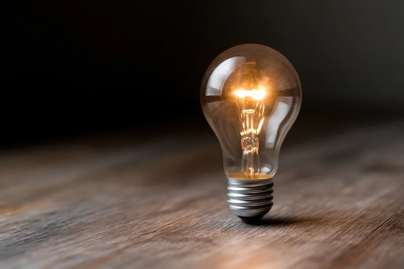 Glowing incandescent light bulb on wooden surface with dark background