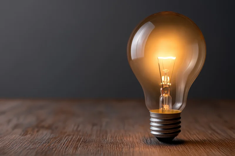 Glowing incandescent light bulb on wooden surface with dark background